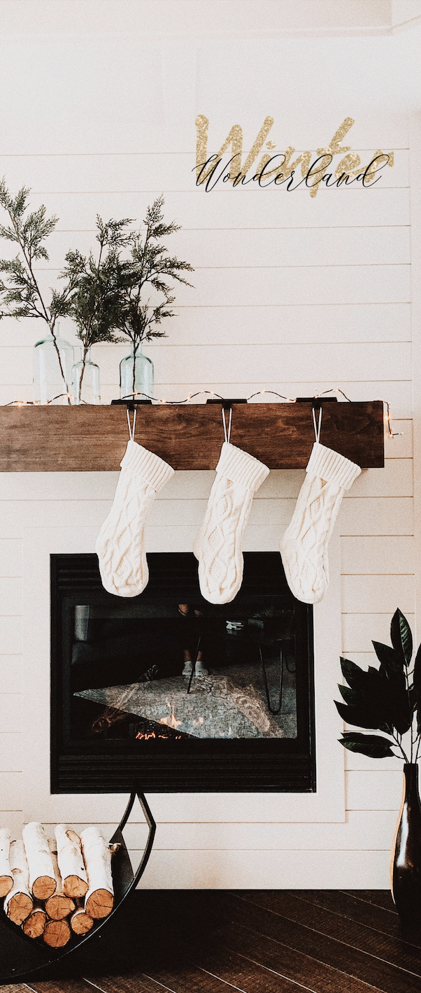 Winter Wonderland Phone Wallpaper with Knit Stockings on the fireplace, plants, and firewood in a cozy home