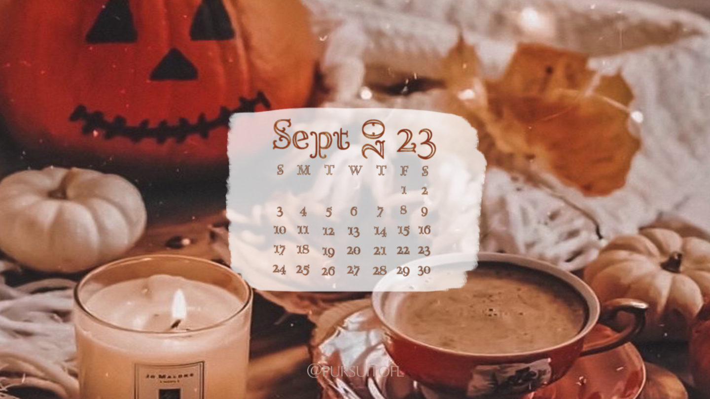 Desktop wallpaper with cozy fall setting with candle, warm drink, fairy lights, pumpkin on a bed, and September 2023 calendar