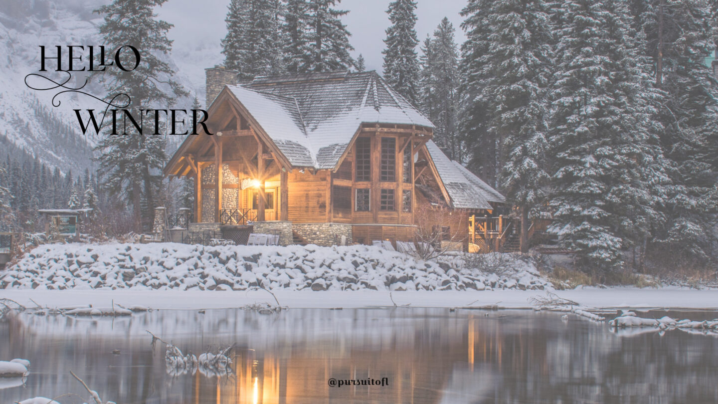 Winter desktop wallpaper with log cabin on a lake in a snowy forest with hello winter text