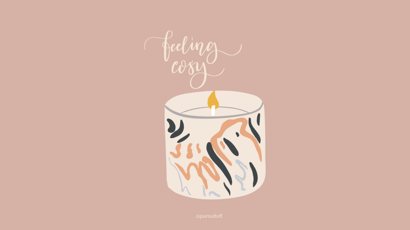 A blush pink desktop wallpaper with an illustration of a lit candle in a white and black marbled holder, with the words 'Feeling Cozy' written in a flowing, script font above.